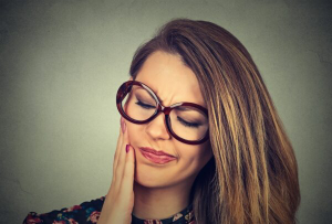 A beautiful woman with eyeglasses is experiencing a toothache