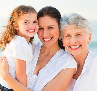 Three generations of smiling women—grandmother, mother, and daughter—embracing outdoors in natural light.