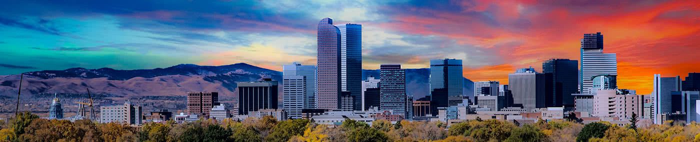 Panoramic view of downtown Denver, Colorado at sunset with the Rocky Mountains in the background — representing Belleview Dental’s local roots in the greater Littleton area.