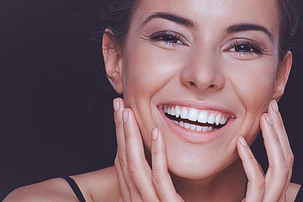 Woman with radiant smile and healthy white teeth touching her face — representing the benefits of professional dental cleanings